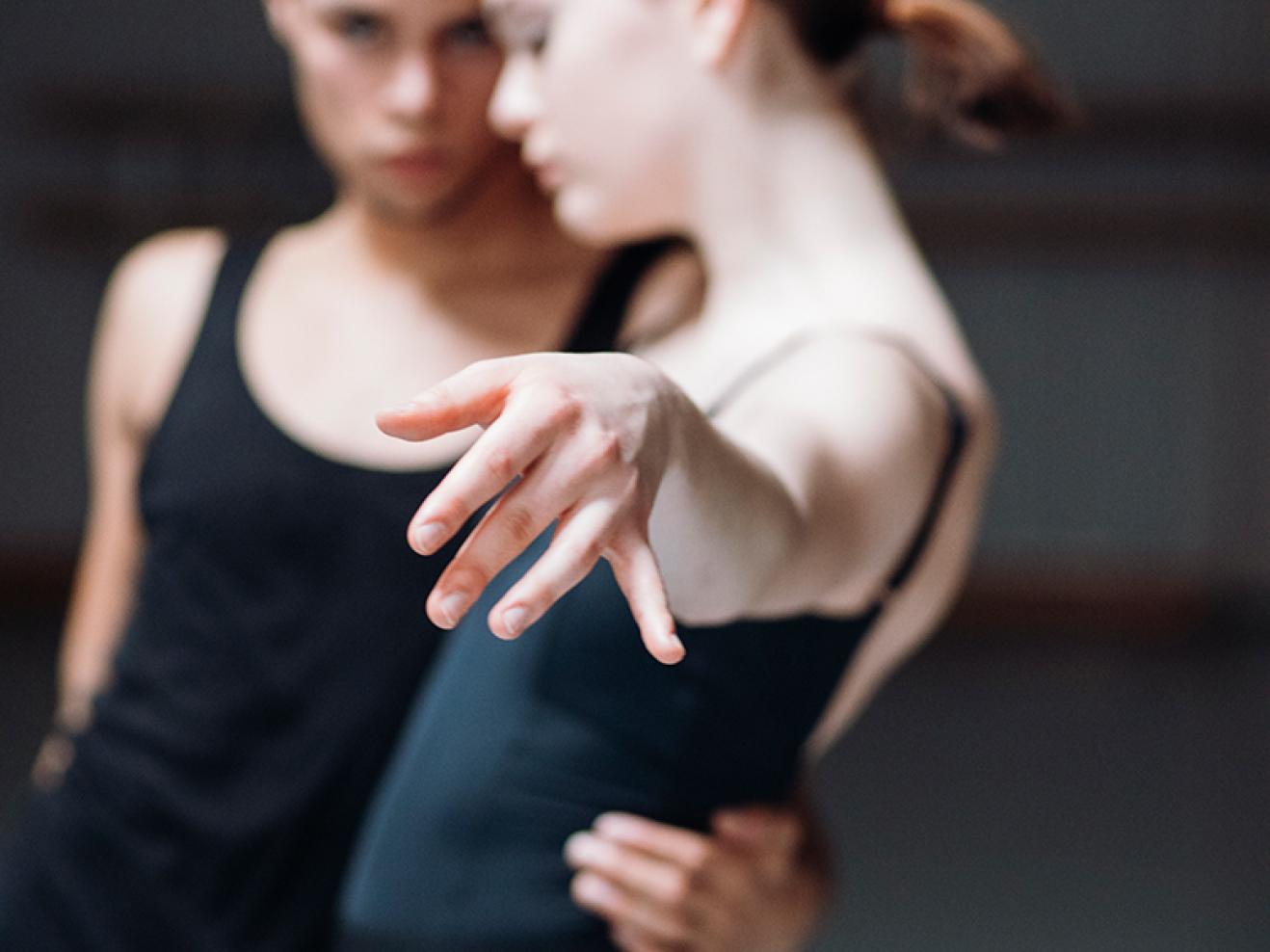 Ein Tänzer hält eine Tänzerin im Arm, sie streckt ihre Hand zur Kamera. Diese ist im Fokus