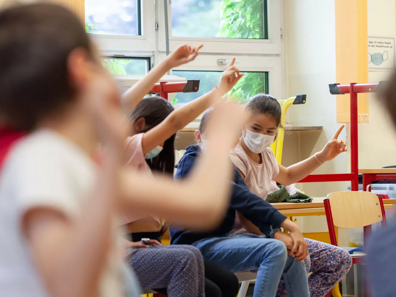 Mehrere Kinder sitzen auf Stühlen und melden sich