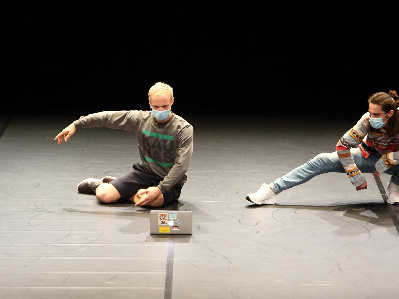 Zwei Tänzer hocken auf dem Boden vor einem aufgeklappten Laptop. Szene aus dem Tanzmarathon 2021.