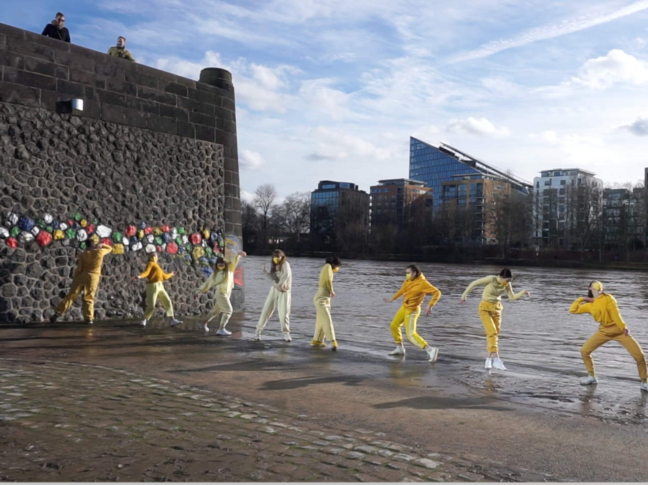 8 tanzende Personen in gelber Kleidung am Mainufer in Frankfurt