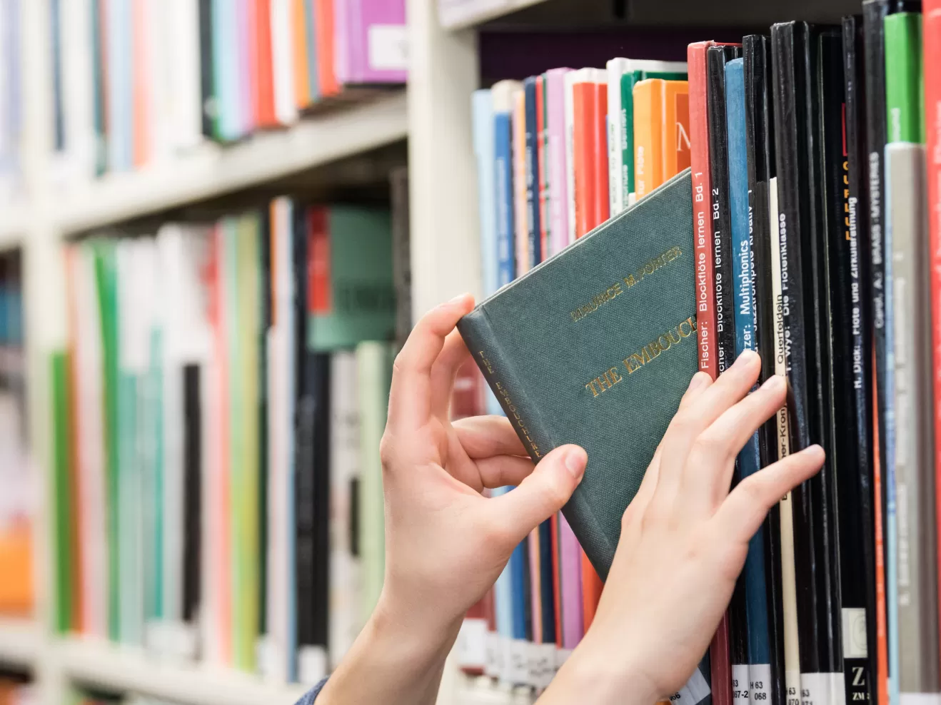 Hände, die ein Buch aus dem Regal nehmen