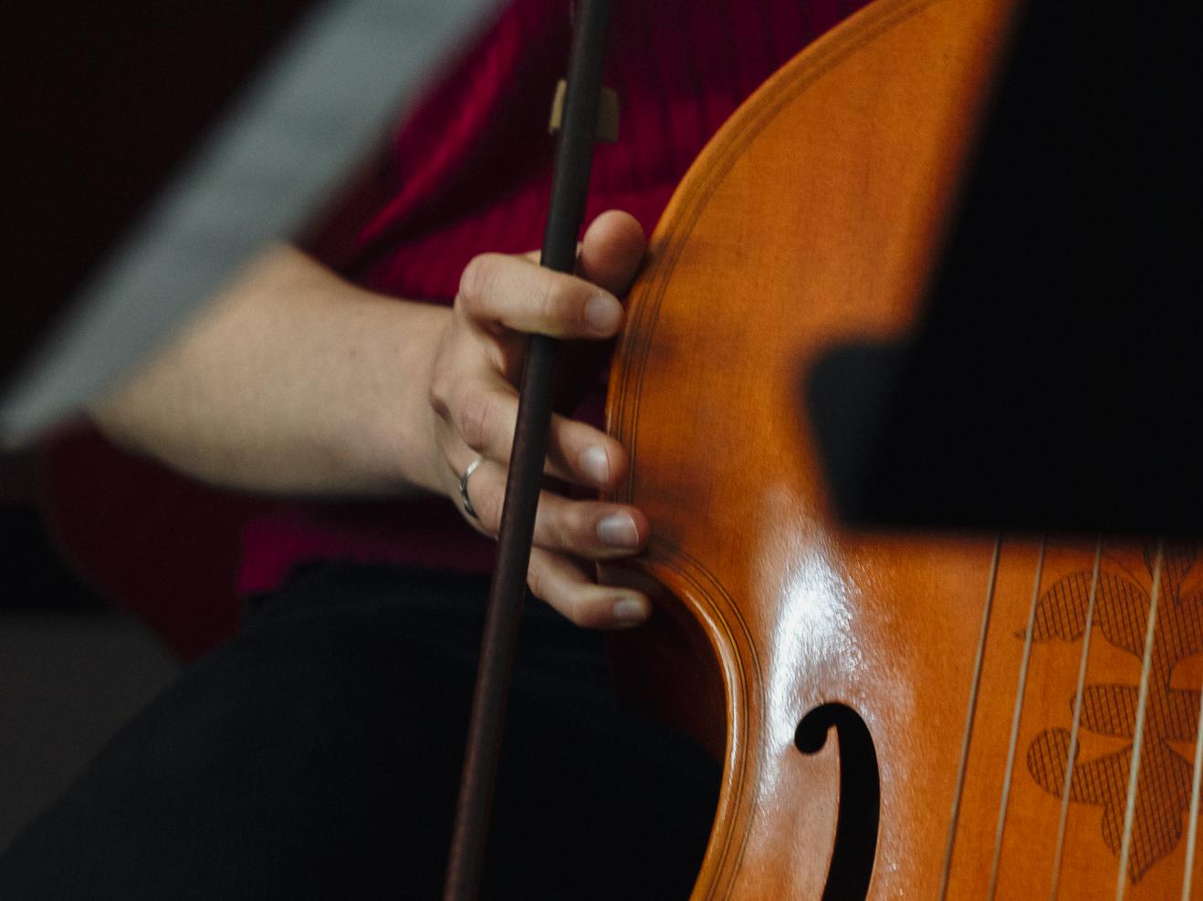 Eine Hand mit Bogen hält ein Barockcello fest