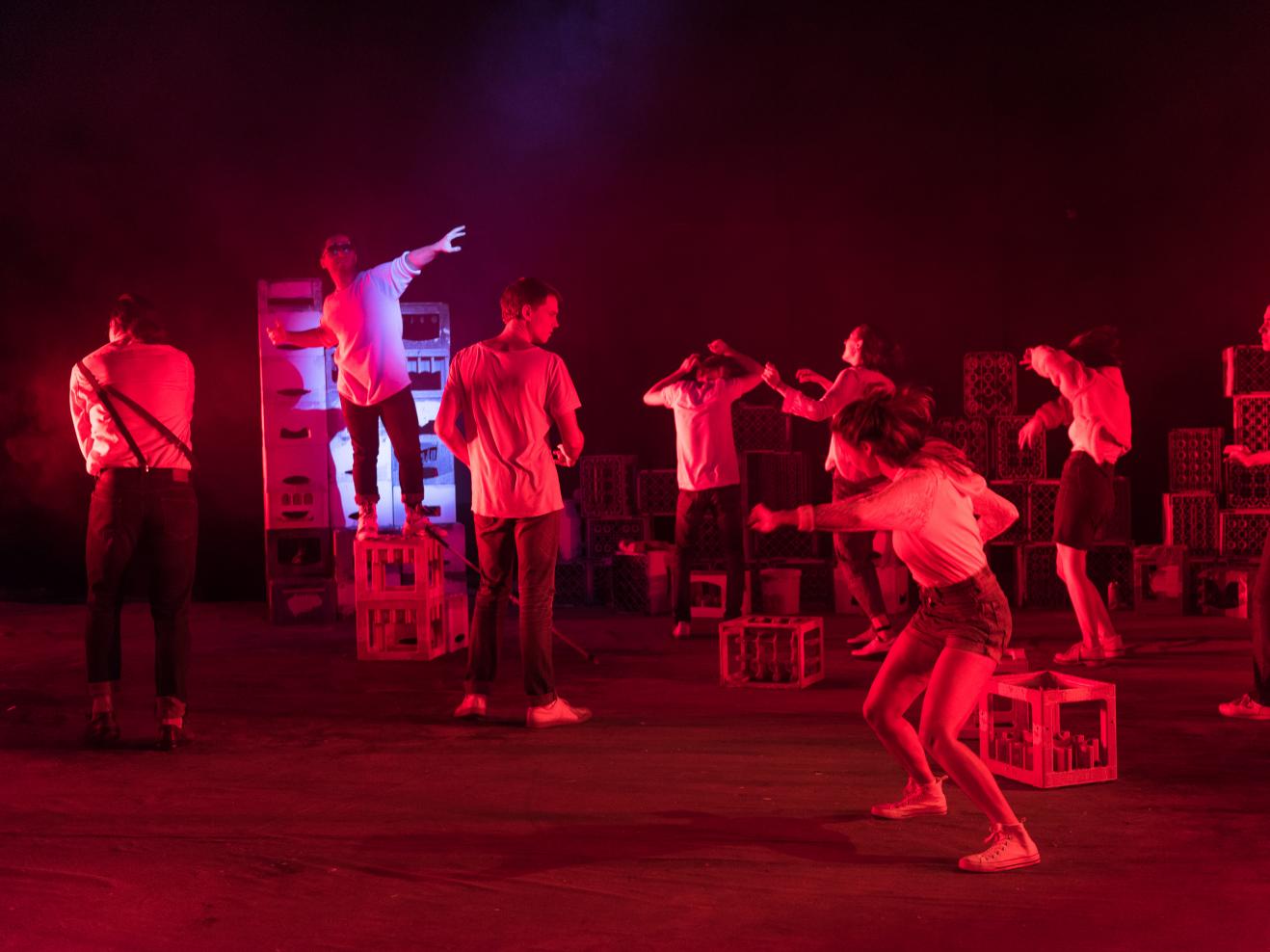 Acht Personen tanzen in rotem Licht auf einer Bühne mit Getränkekästen