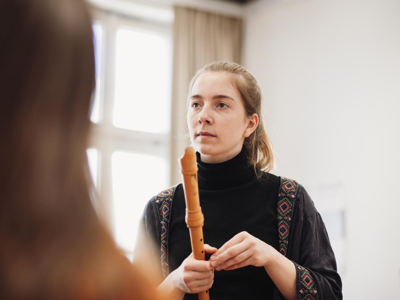 Eine Studentin hält ihre Blockflöte in der Hand, ist einer anderen Person zugewandt, die man nicht sehen kann