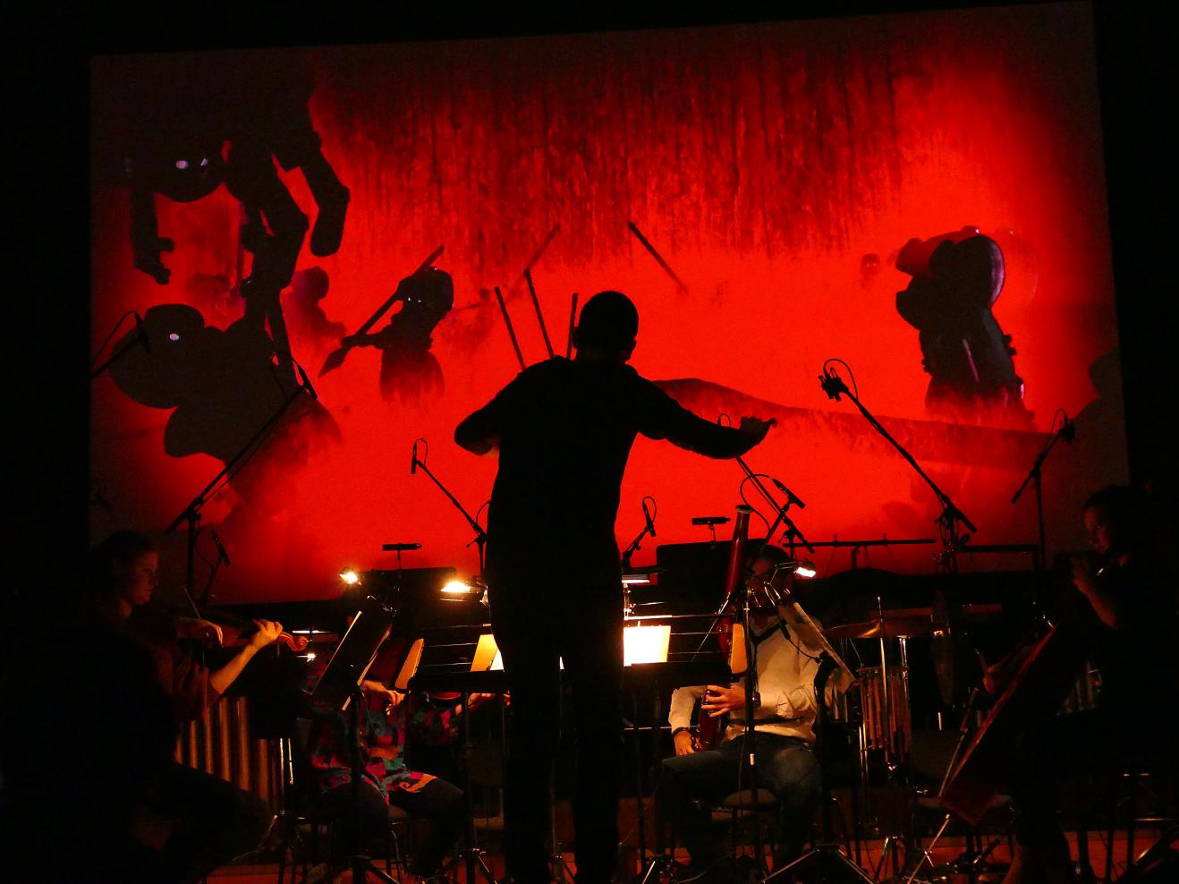 Ein Dirigent leitet ein Orchester mit Livemusik zu einem Stummfilm