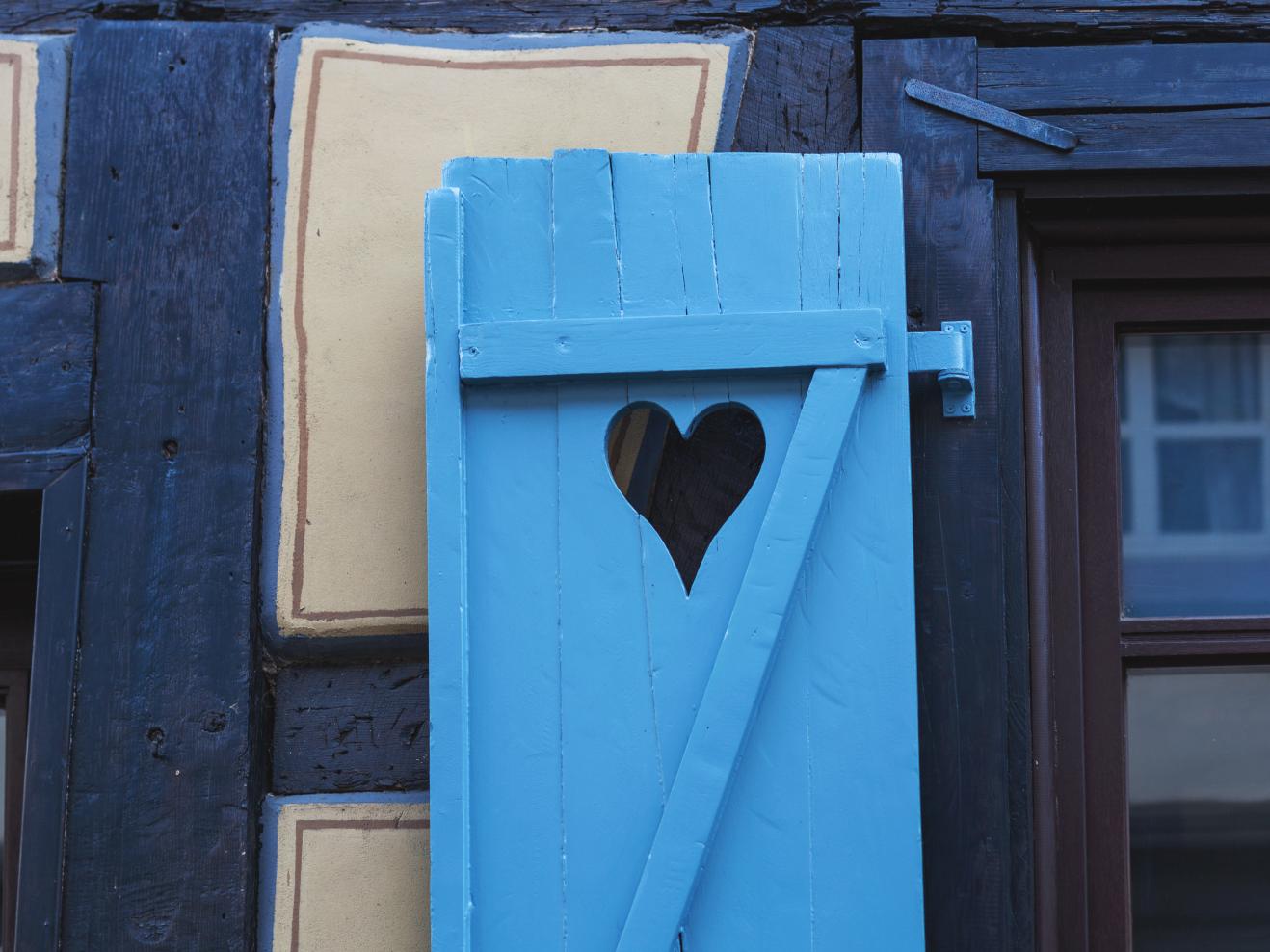 Ein blauer Fensterladen an einem Fachwerkhaus mit einem herzförmigen Ausschnitt