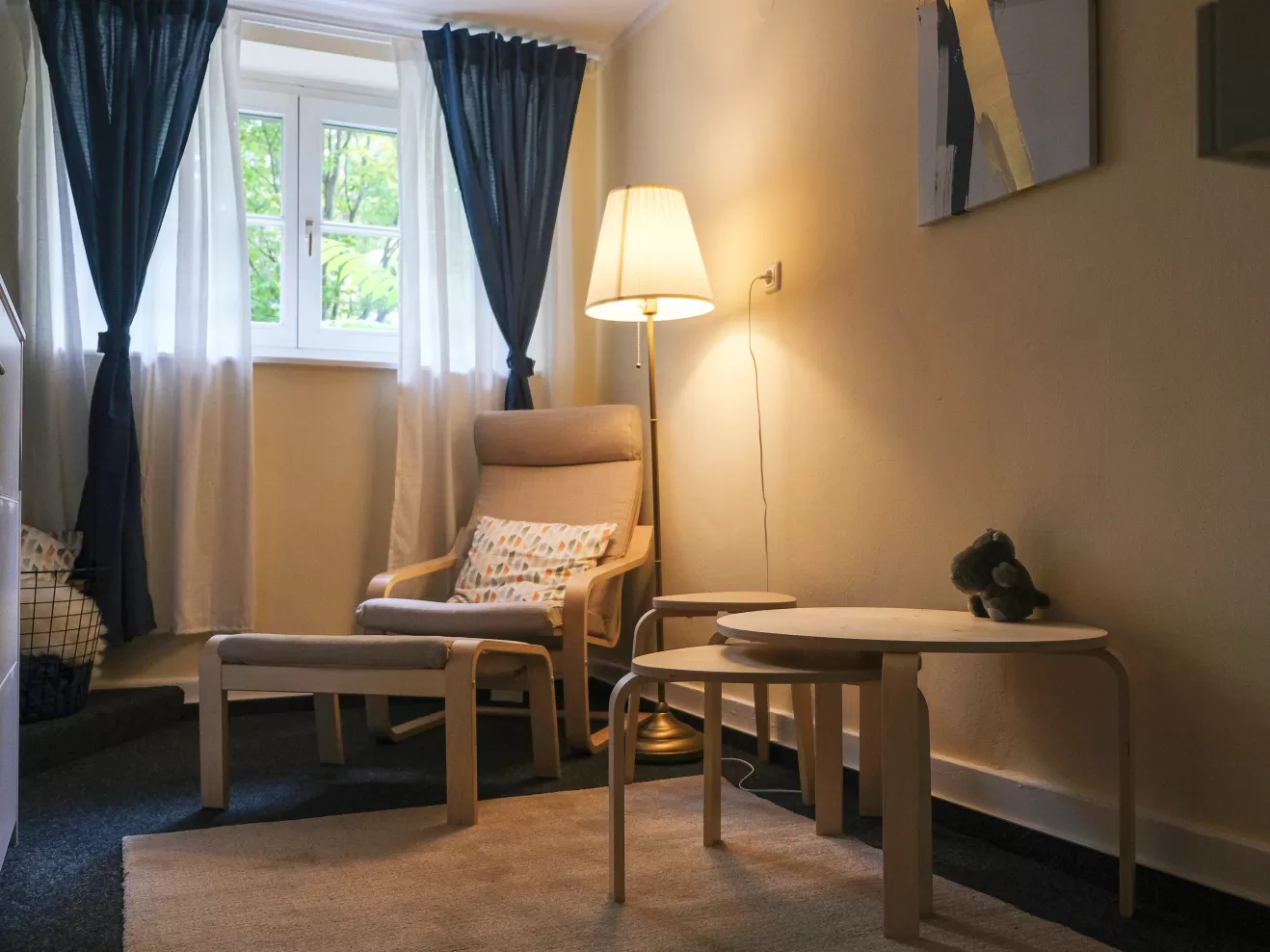 Eltern-Kind-Raum mit Sessel, Teppich und einer Stehlampe, die gemütliches Licht ausstrahlt.
