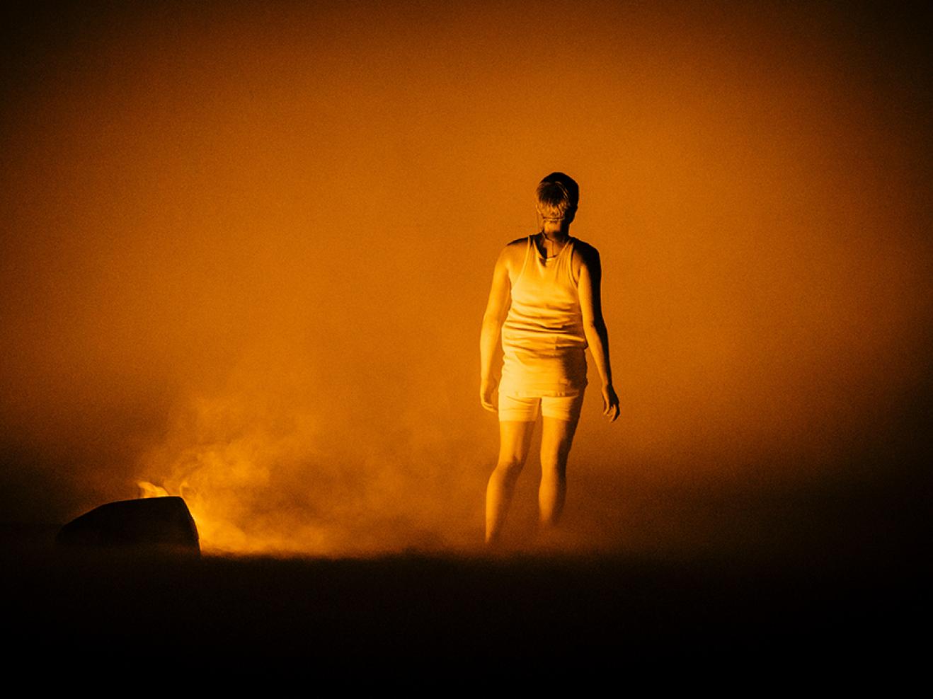 Eine Person, von hinten gesehen, auf der Bühne in gelbem Nebel.