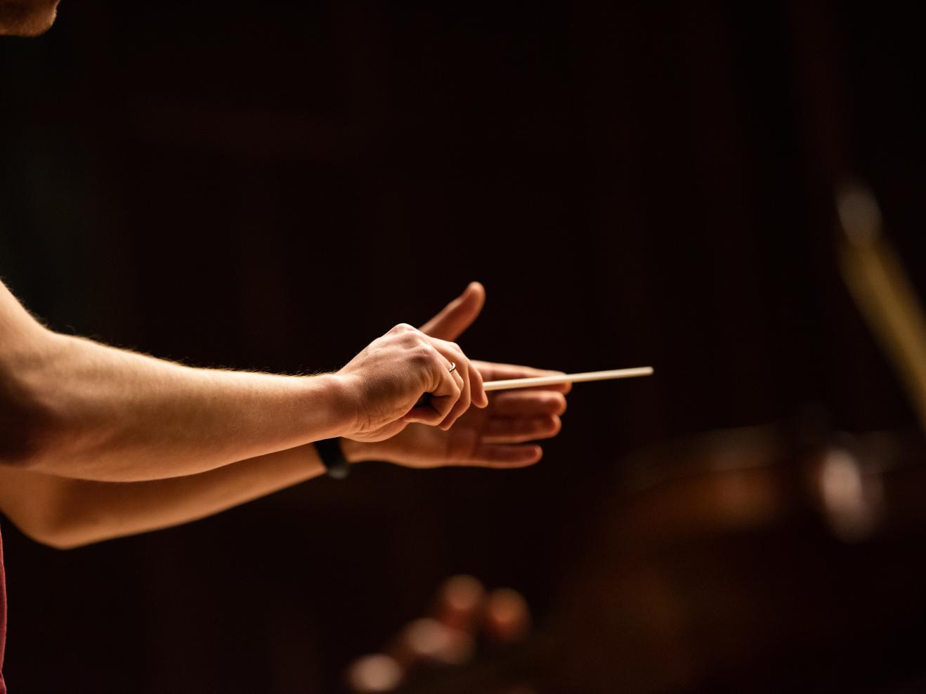 Nahaufnahme der Hände eines Dirigenten mit Taktstock.