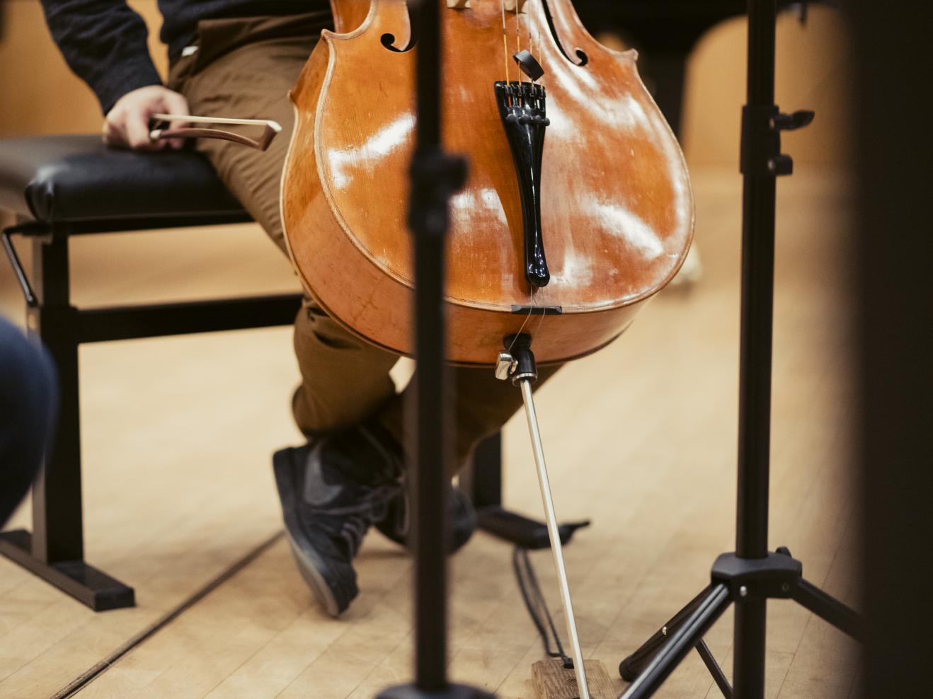 Cellist (man sieht nur die untere Hälfte seines Instruments und seine Hände), die Hand am Bogen angespannt.