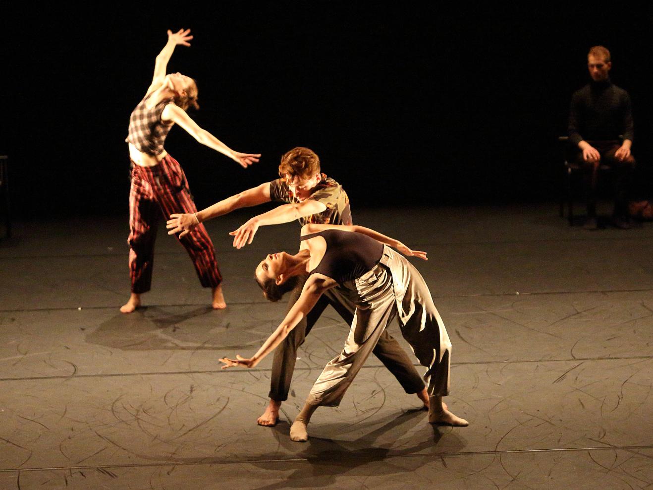 Drei Tanzenden bewegen sich auf der Bühne im Scheinwerferlicht