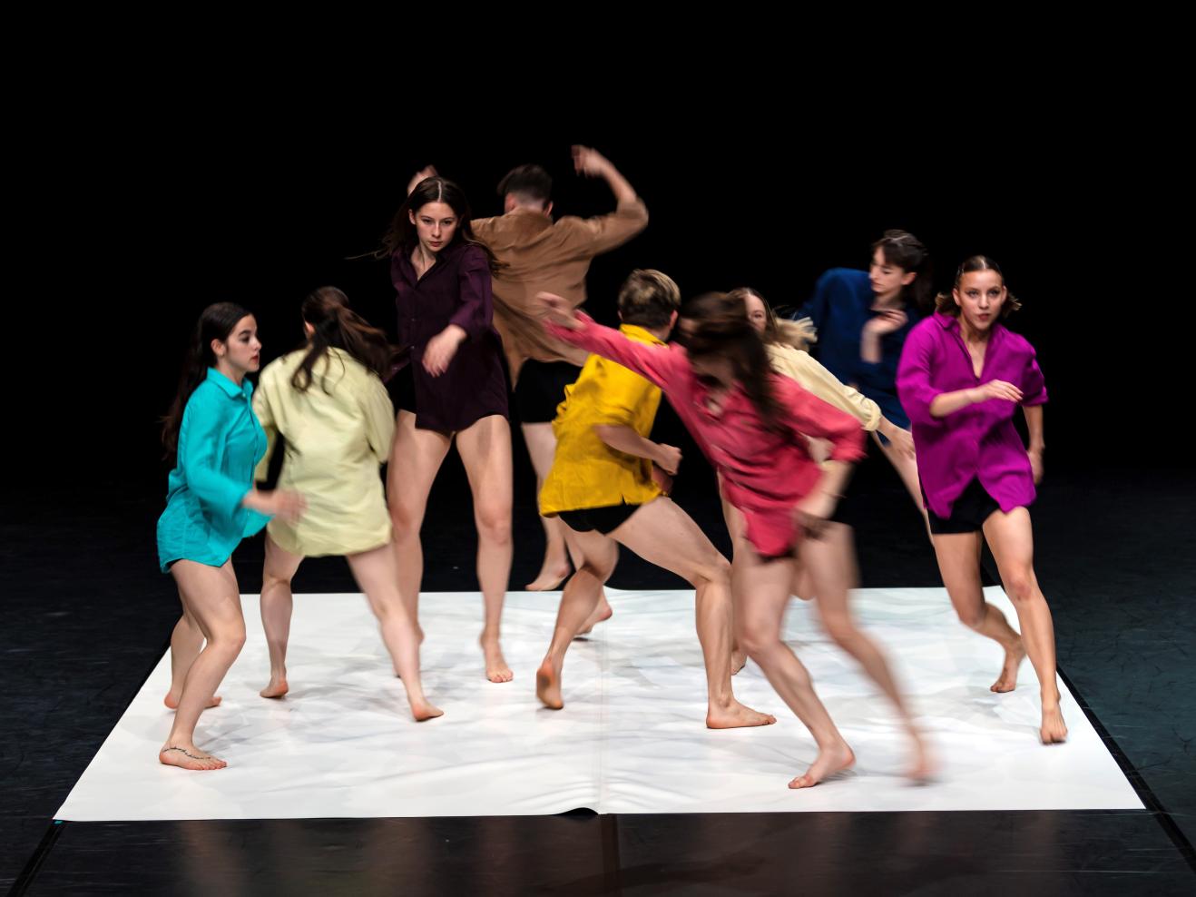 Gruppe von 8 Tänzer*innen in bunten Hemden, in dynamischer Bewegung fotografier.