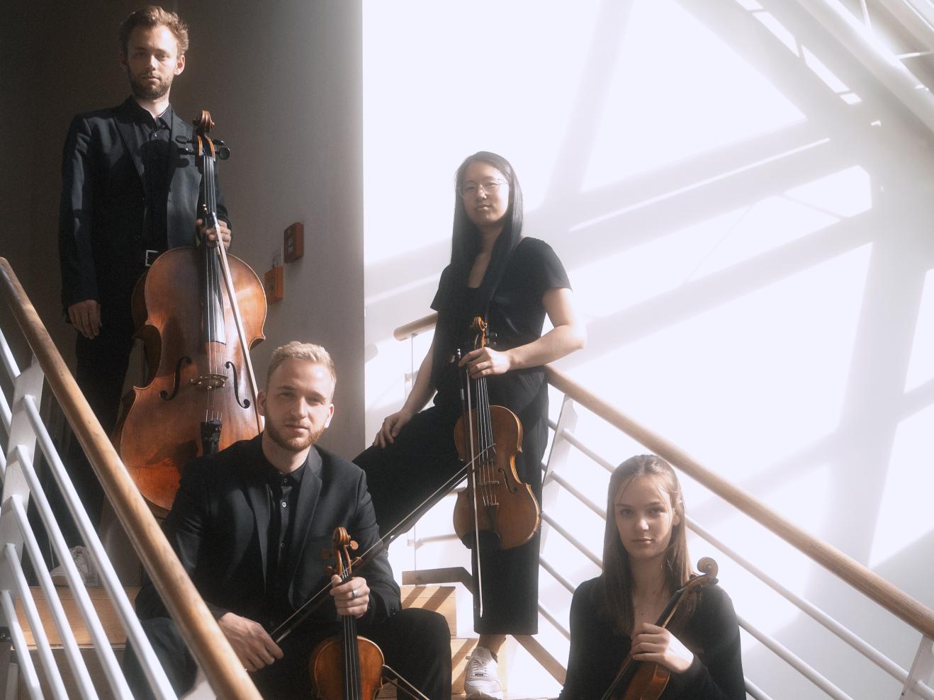 Die vier Musiker*innen des Eunoia Quartett sitzen auf einer Holztreppe mit ihren Instrumenten.