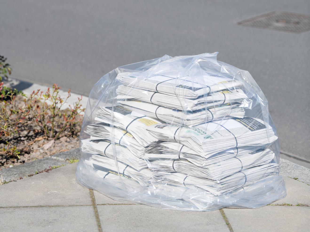 Ein in durchsichtige Plastikfolie gehüllter Stapel von Zeitungen liegt auf einem Bürgersteig in Frankfurt.