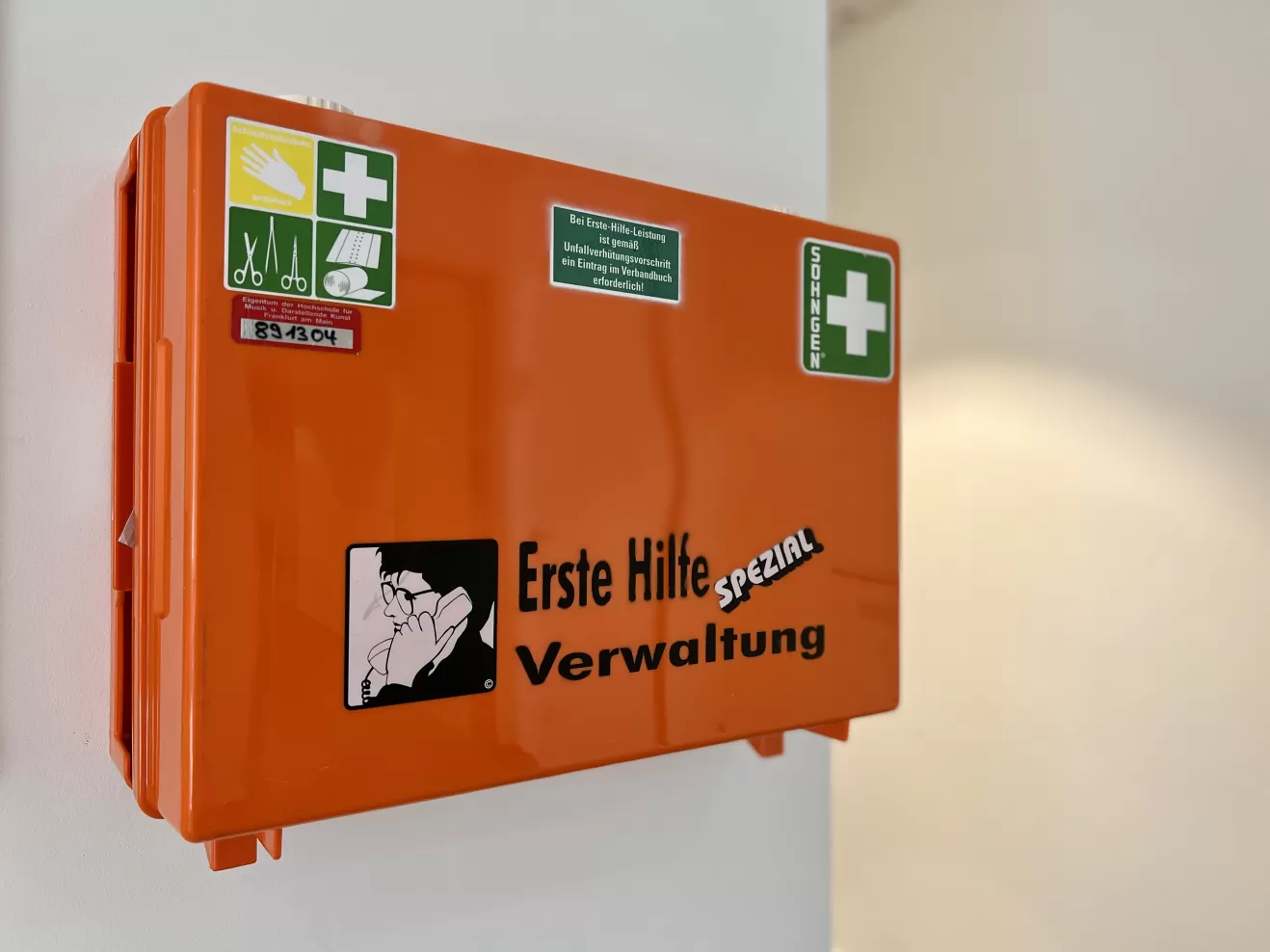 Ein orangener Erste-Hilfe-Koffer, der an einer weißen Wand hängt.
