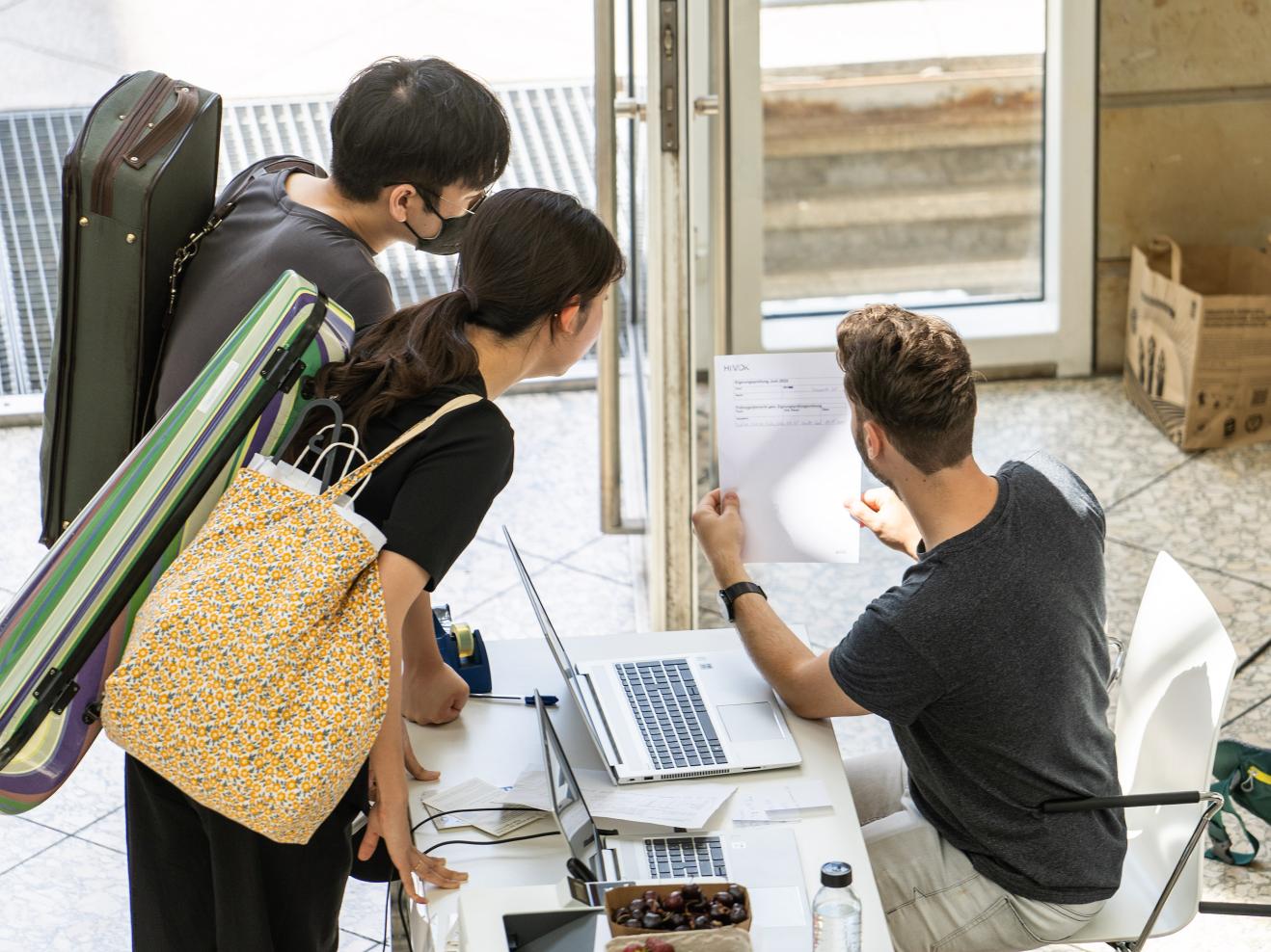 Zwei Studienbewerber*innen werden im Foyer der HfMDK von einem studentischen Mitarbeiter zur Eignungsprüfung beraten.