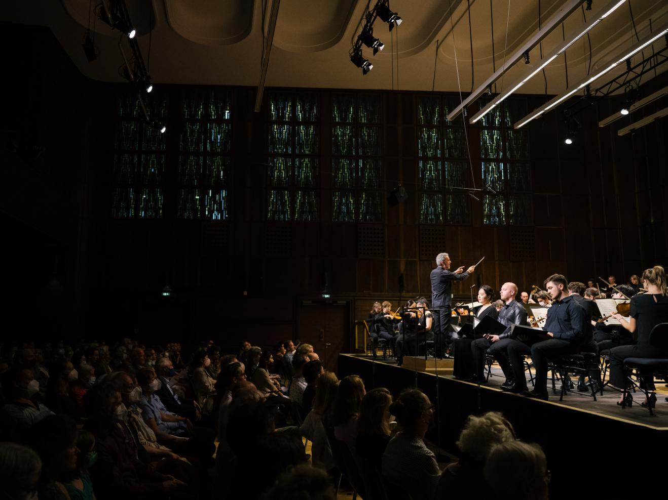 Orchesterkonzert im Großen Saal der HfMDK, Aufnahme von der Seite: Das Publikum ist links im Bild zu sehen, rechts die Bühne mit den Musiker*innen.