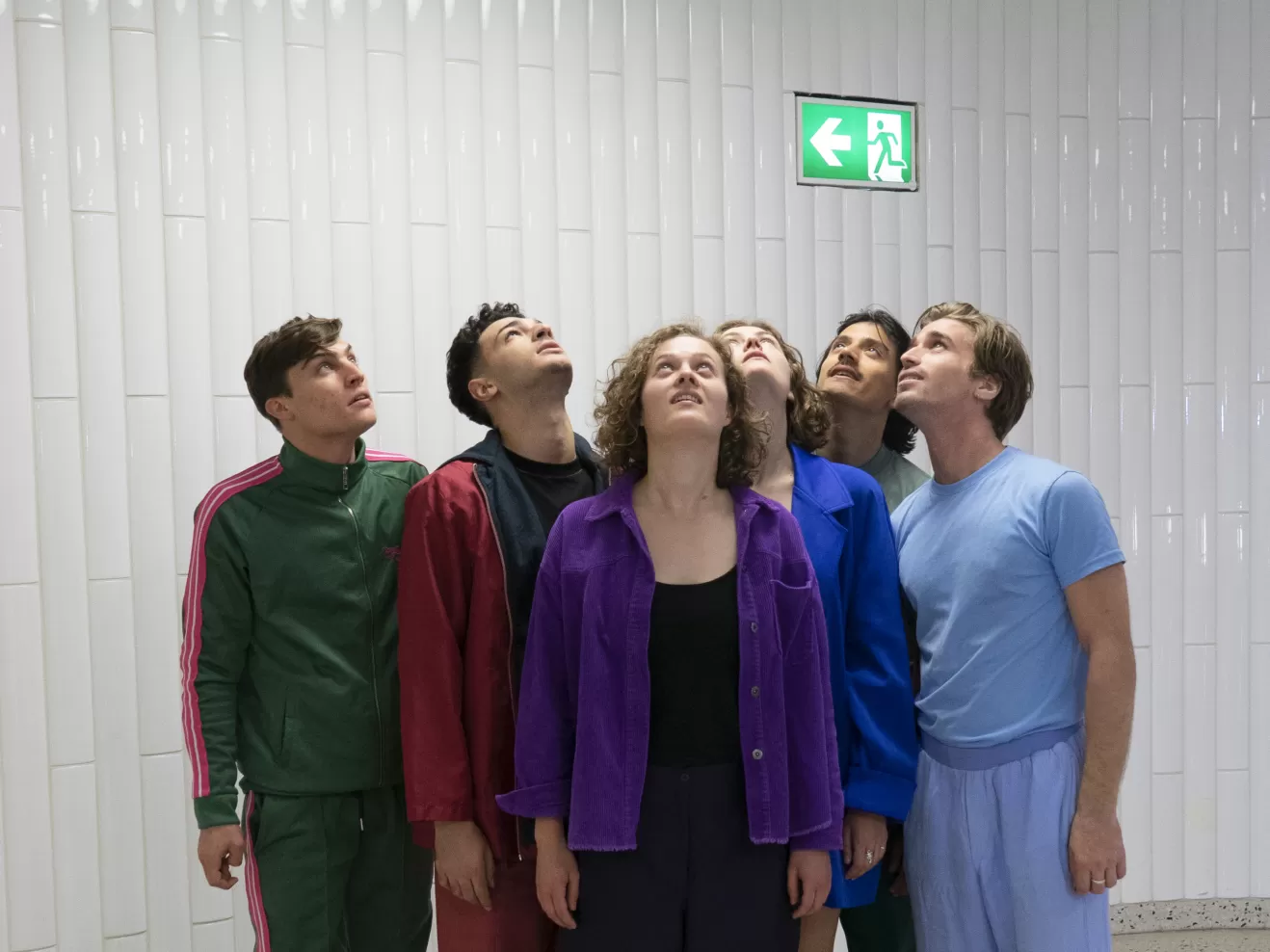 Sechs Schauspielabsolvierende nebeneinander, den Blick nach oben zu einem Notausgangsschild gerichtet.