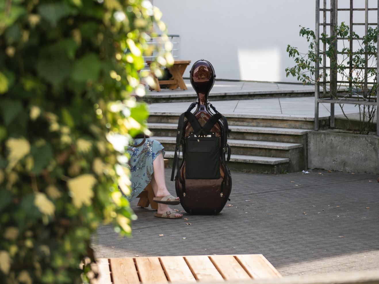 Ein Cellokasten steht neben einer sitzenden Person im Innenhof