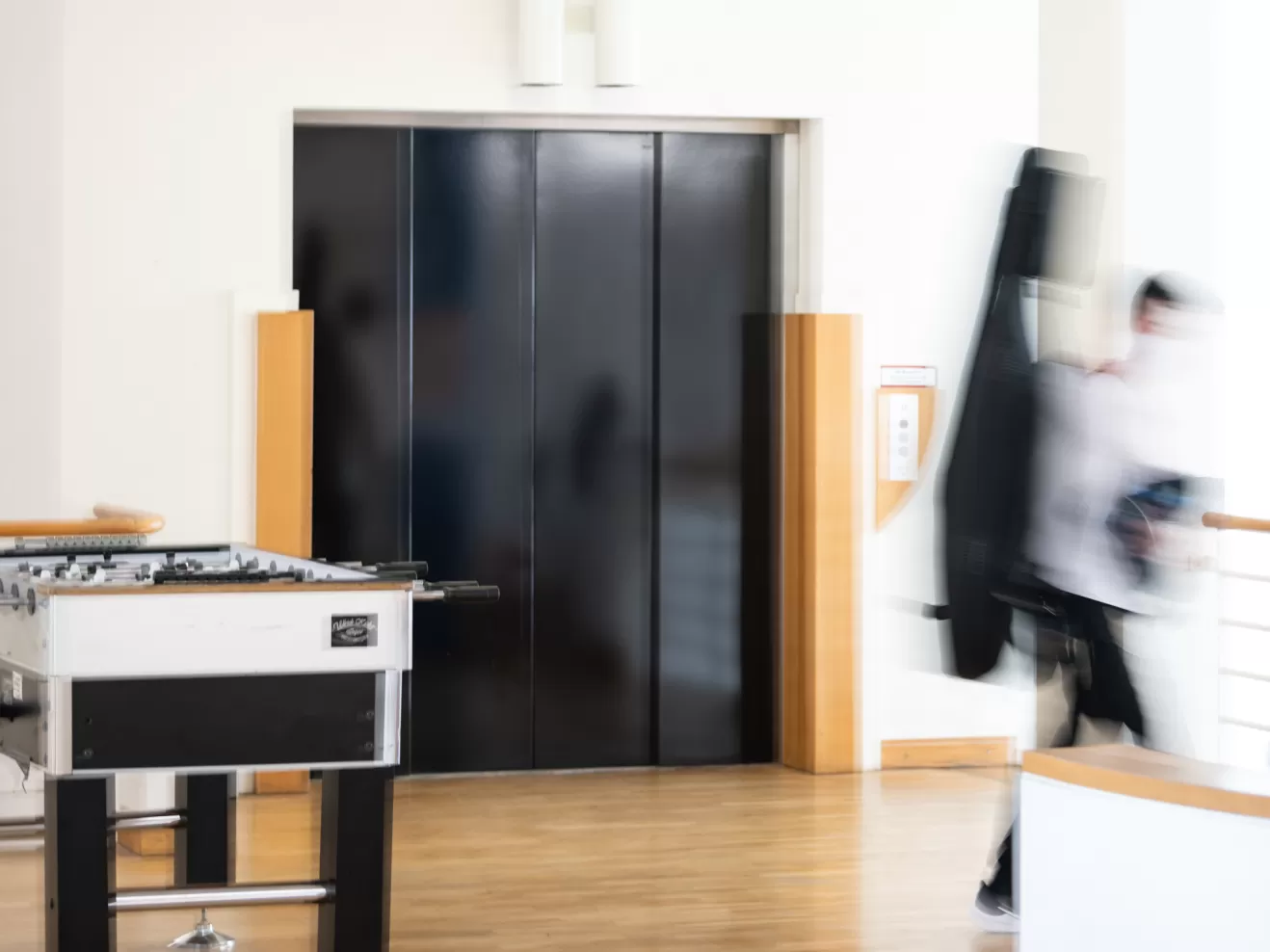 Aufzugstür, Kickertisch und eine verschwommene Person mit Cellokasten auf dem Rücken