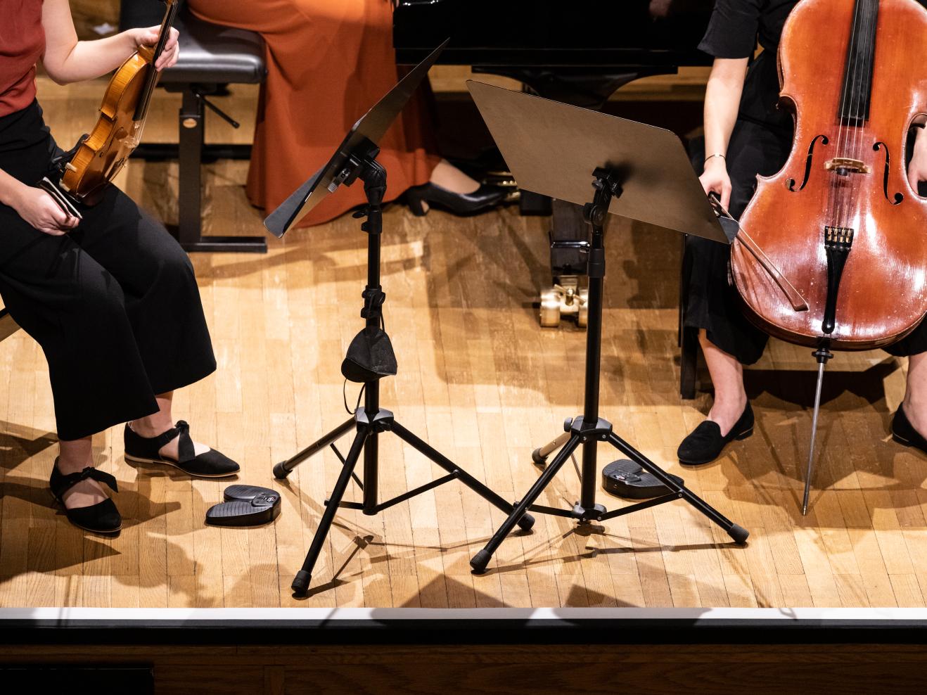 Bildausschnitt eines Kammermusik-Trios: Füße, Hände und Instrumente.