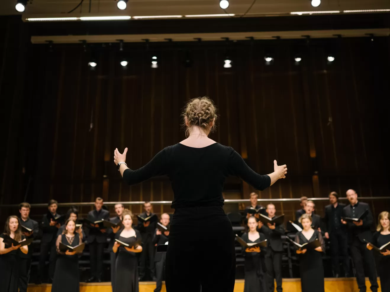 Rückenansicht einer Studierenden, die einen Chor dirigiert.