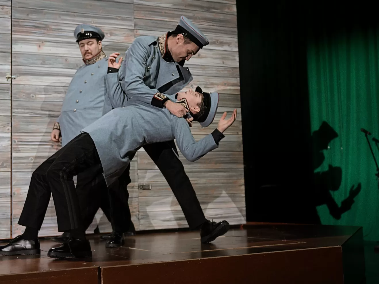 Drei uniformierte Männer, einer hält einen zweiten am Kragen fest.