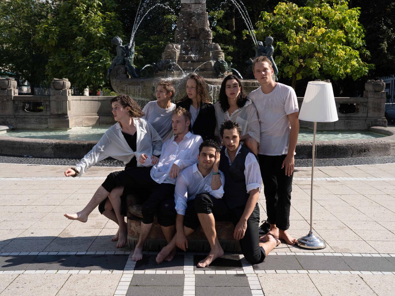 Absolvierende Schauspiel auf einem Sofa, alle nass, vor einem großen Springbrunnen.