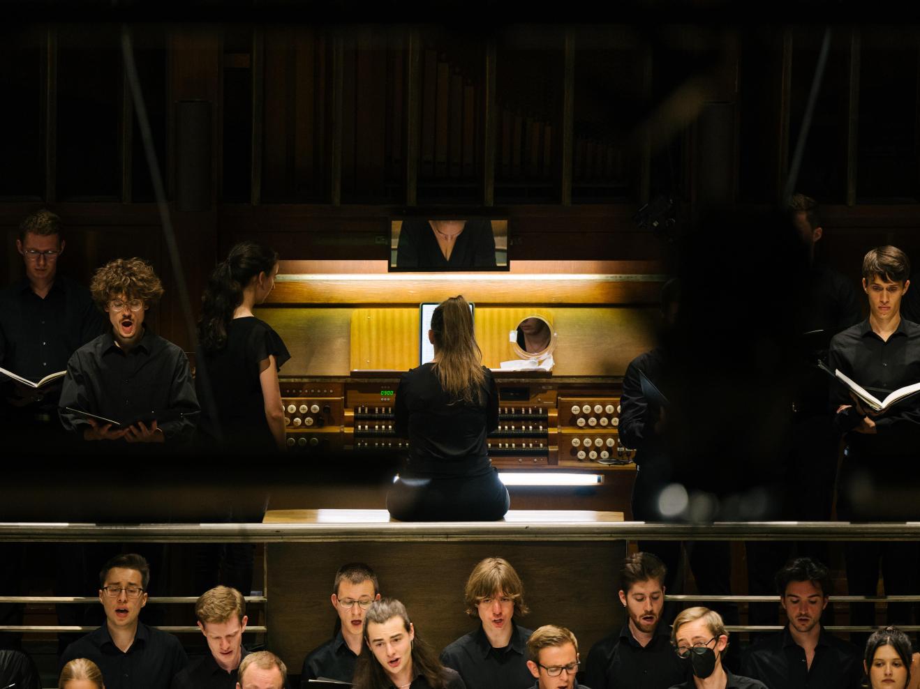 Organistin an der Orgel im Großen Saal der HfMDK, davor und daneben Chorsänger*innen.