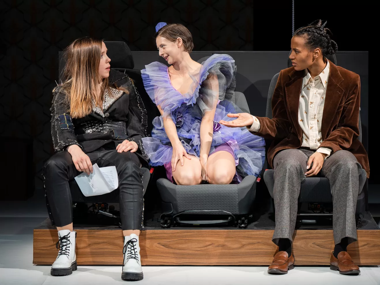 Drei Schauspielerinn sitzen auf ausgebauten Autositzen und unterhalten sich.