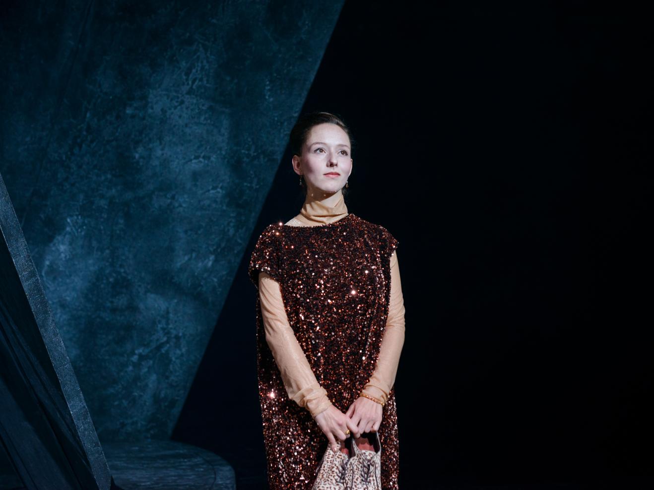 Schauspielerin in einem Paillettenkleid und mit ihren Schuhen in der Hand schaut verträumt.