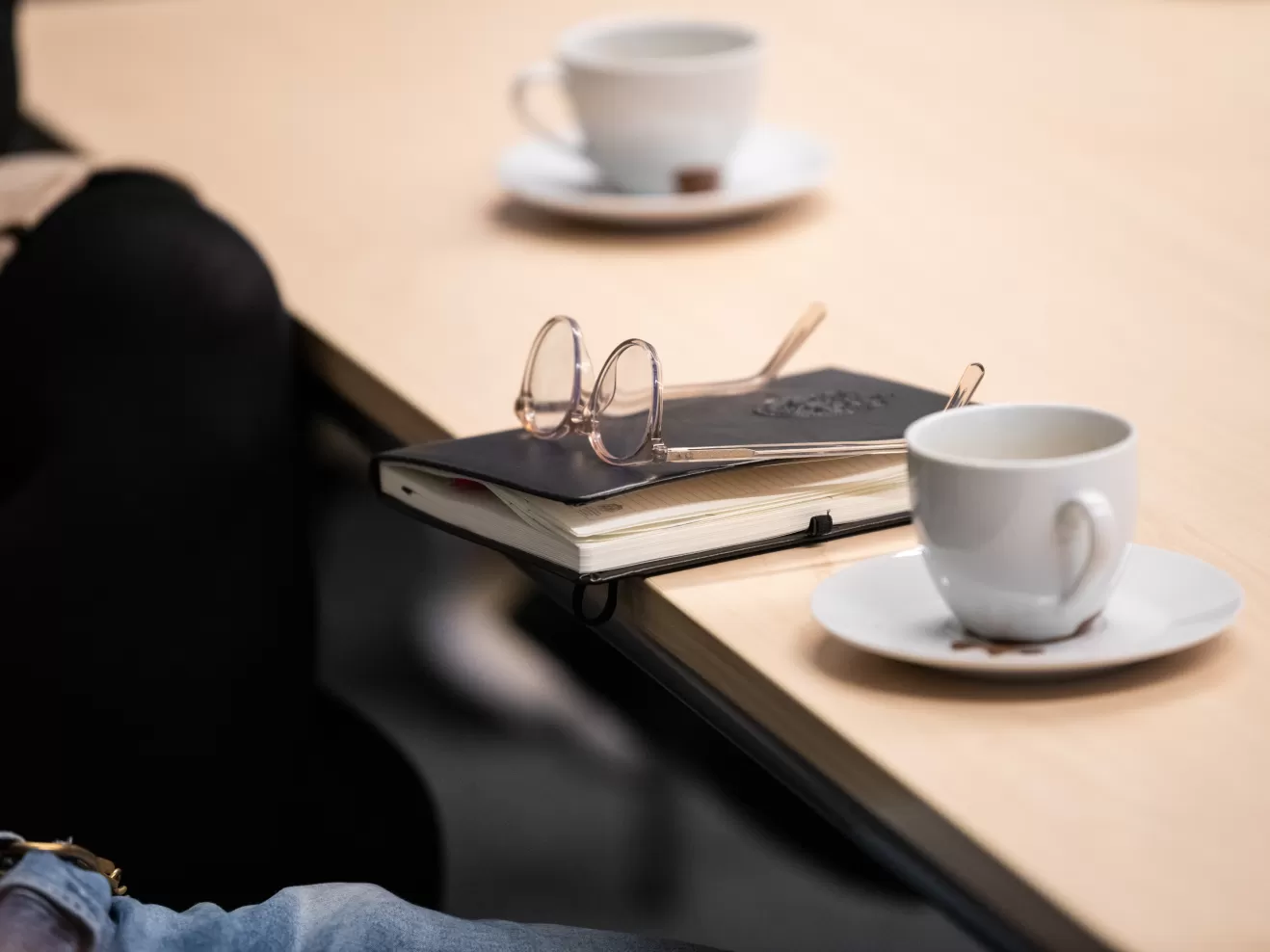 Zwei Kaffeetassen und ein Notizbuch mit einer darauf abgelegten Brille