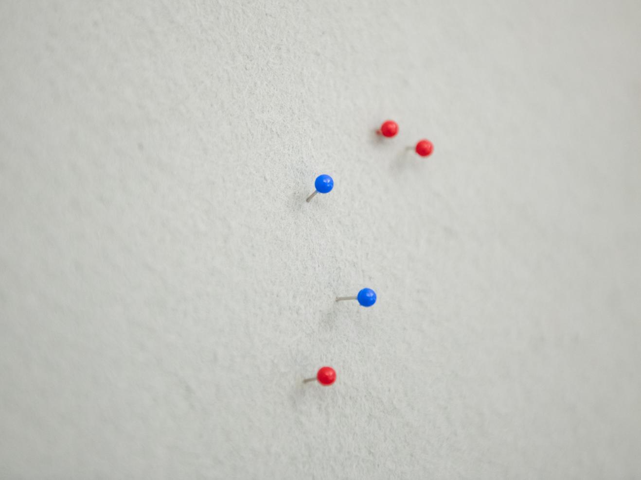 Stecknadeln mit blauen und roten Köpfen in einer weißen Pinnwand