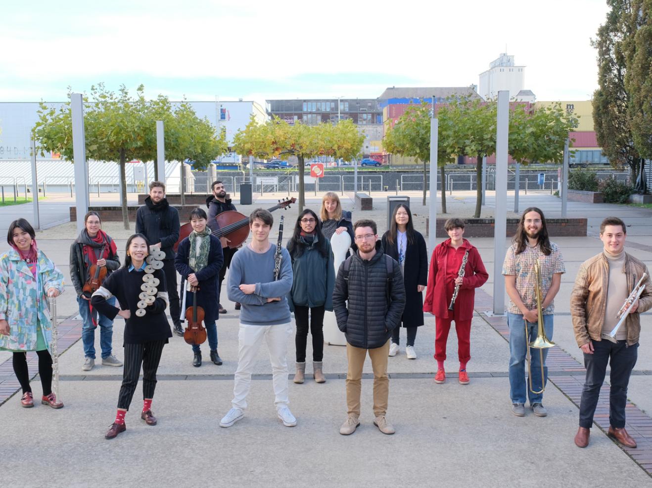 14 Musiker*innen des IEMA-Ensembles stehen am Osthafen Frankfurt.