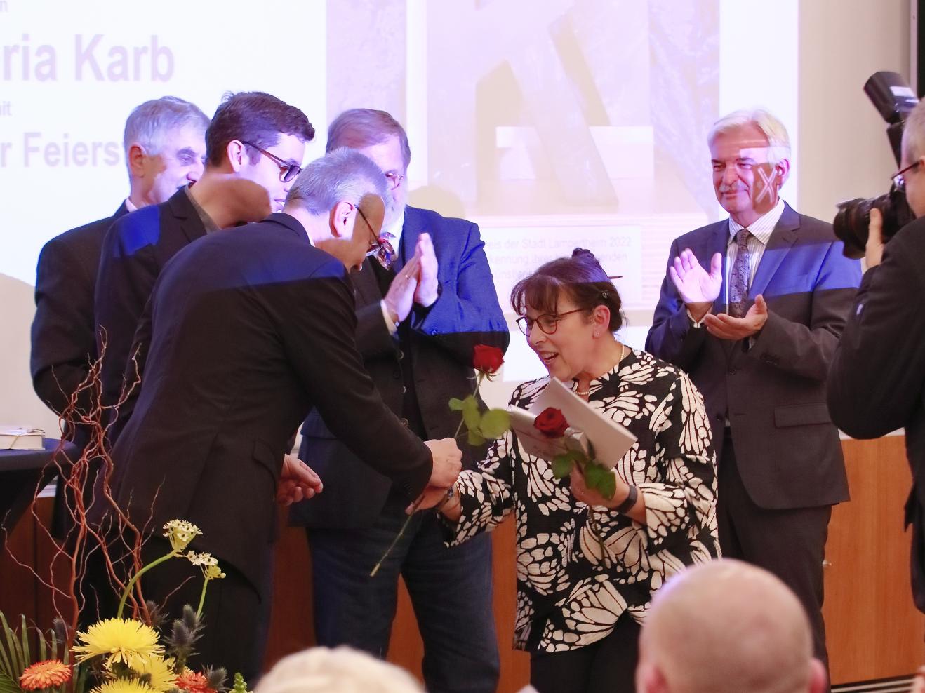 Applaudierende Menschen, eine Maria Karb in der Mitte erhält Rosen 