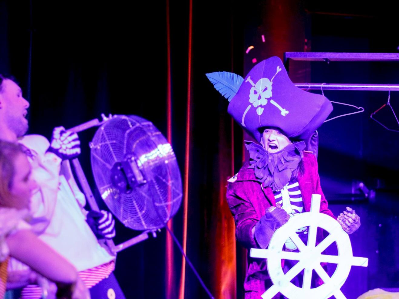 Pirat mit Steuerrad, ein Schauspieler bläst ihr mit einem Ventilator Wind entgegen.