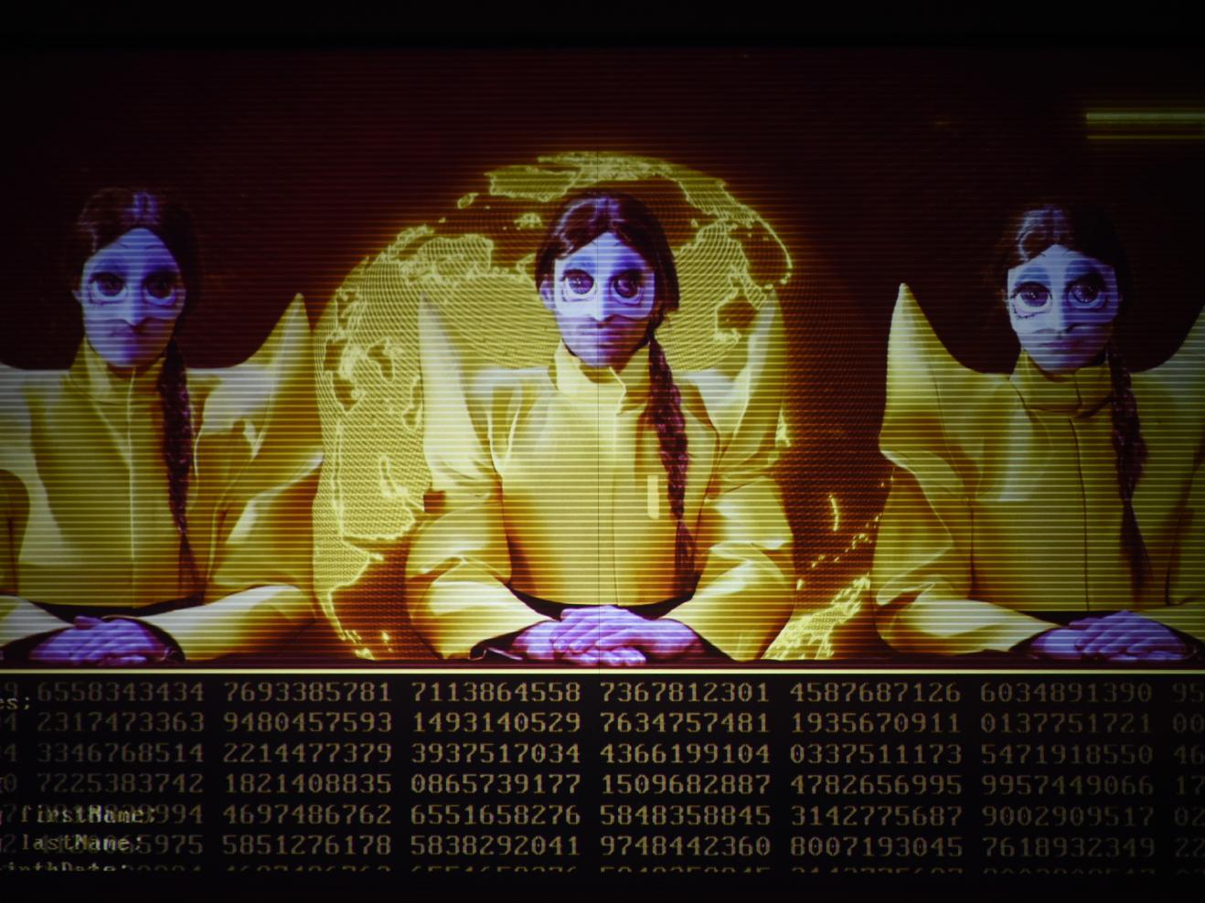 Drei gelb gekleidetet und maskierte Personen sitzen vor einer digitalen Weltkugel.