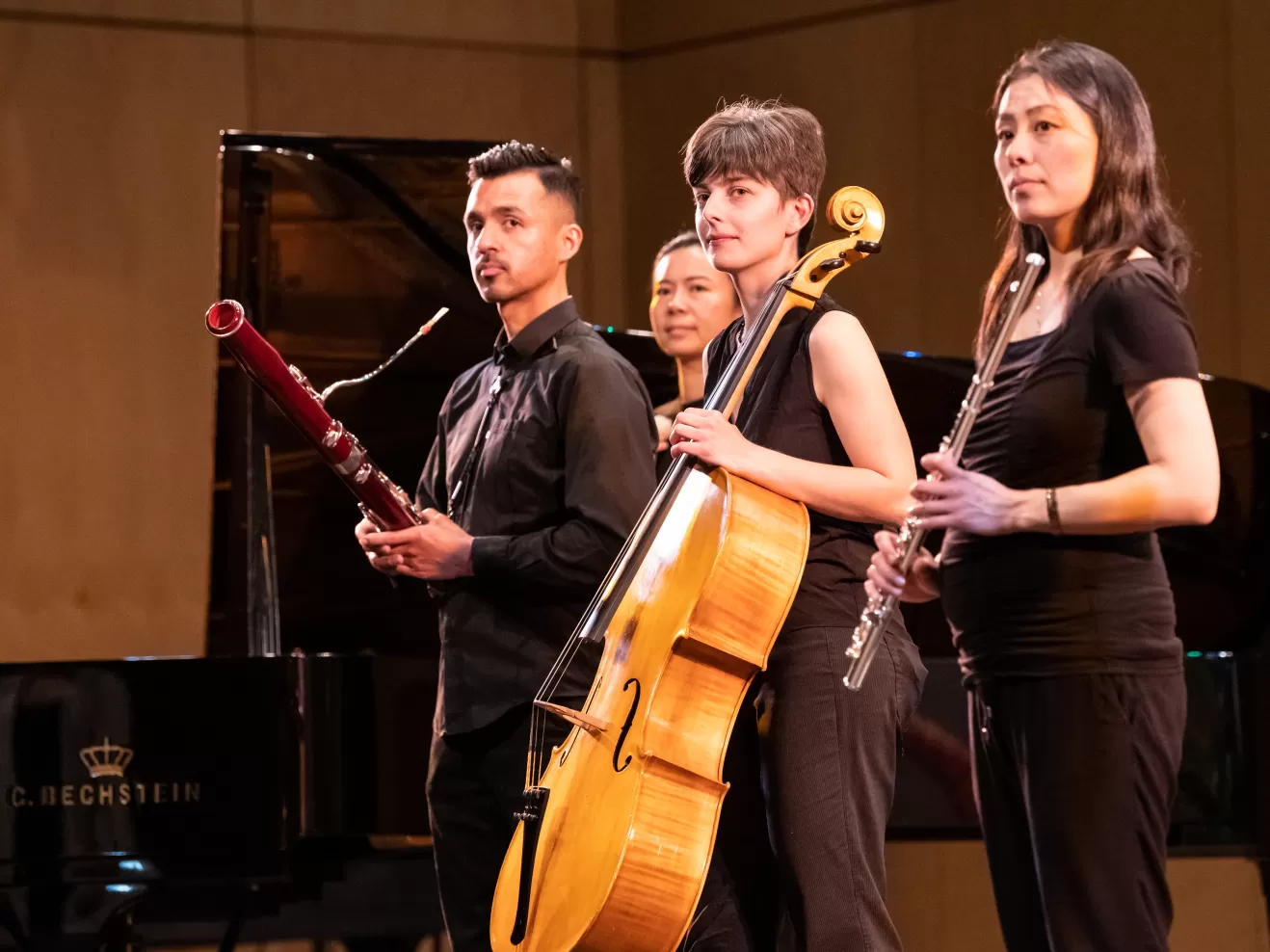 Musiker*innen mit ihren Instrumenten (Fagott, Cello, Querflöte) stehen auf der Bühne im Kleinen Saal der HfMDK und blicken schräg links nach vorne in die Kamera.