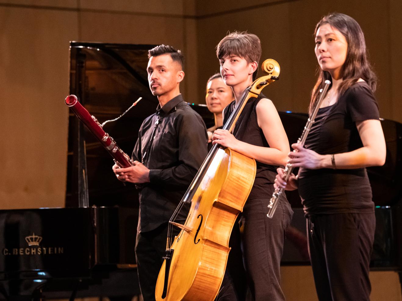 Musiker*innen mit ihren Instrumenten (Fagott, Cello, Querflöte) stehen auf der Bühne im Kleinen Saal der HfMDK und blicken schräg links nach vorne in die Kamera.