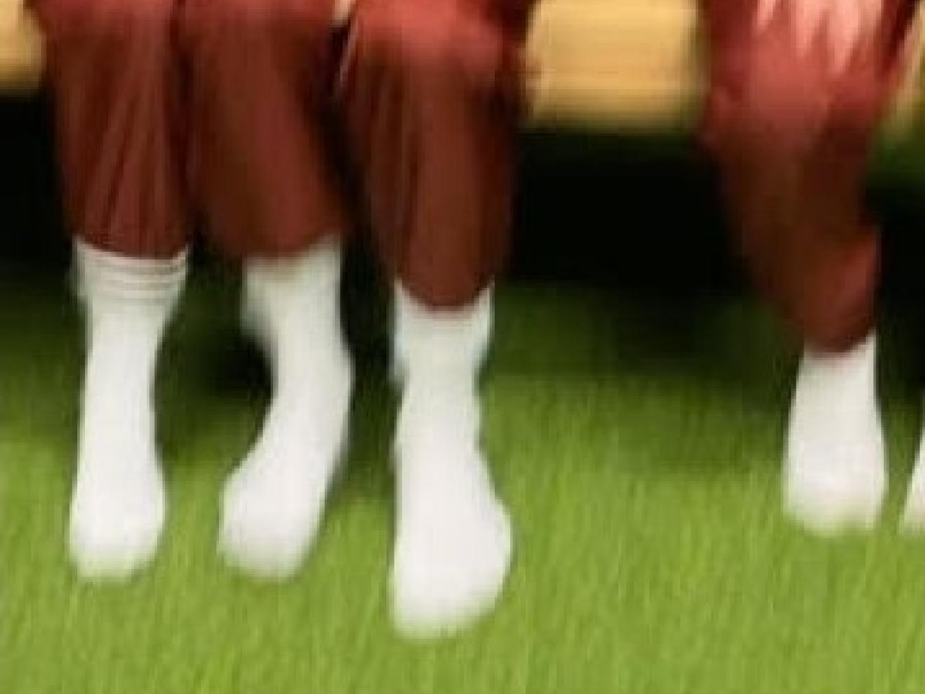 Unscharfer Blick auf drei Personen, die auf einer Holzbank sitzen und von denen nur die Beine und Füsse zu sehen sind und die rote Hosen und weisse Socken tragen.