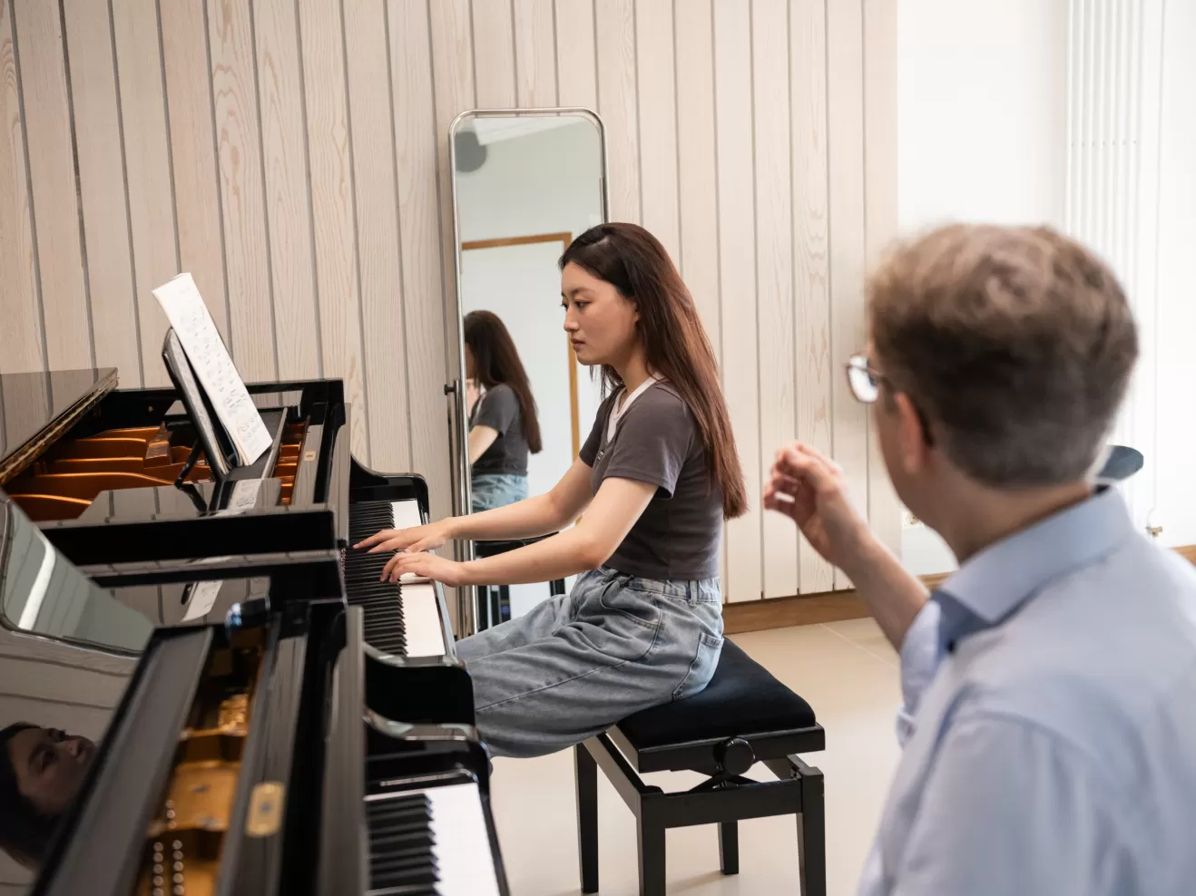 Klavier-Einzelunterricht: Eine Studentin spielt am Flügel, im Vordergrund sieht man den Professor, der ihr währenddessen etwas erklärt. 