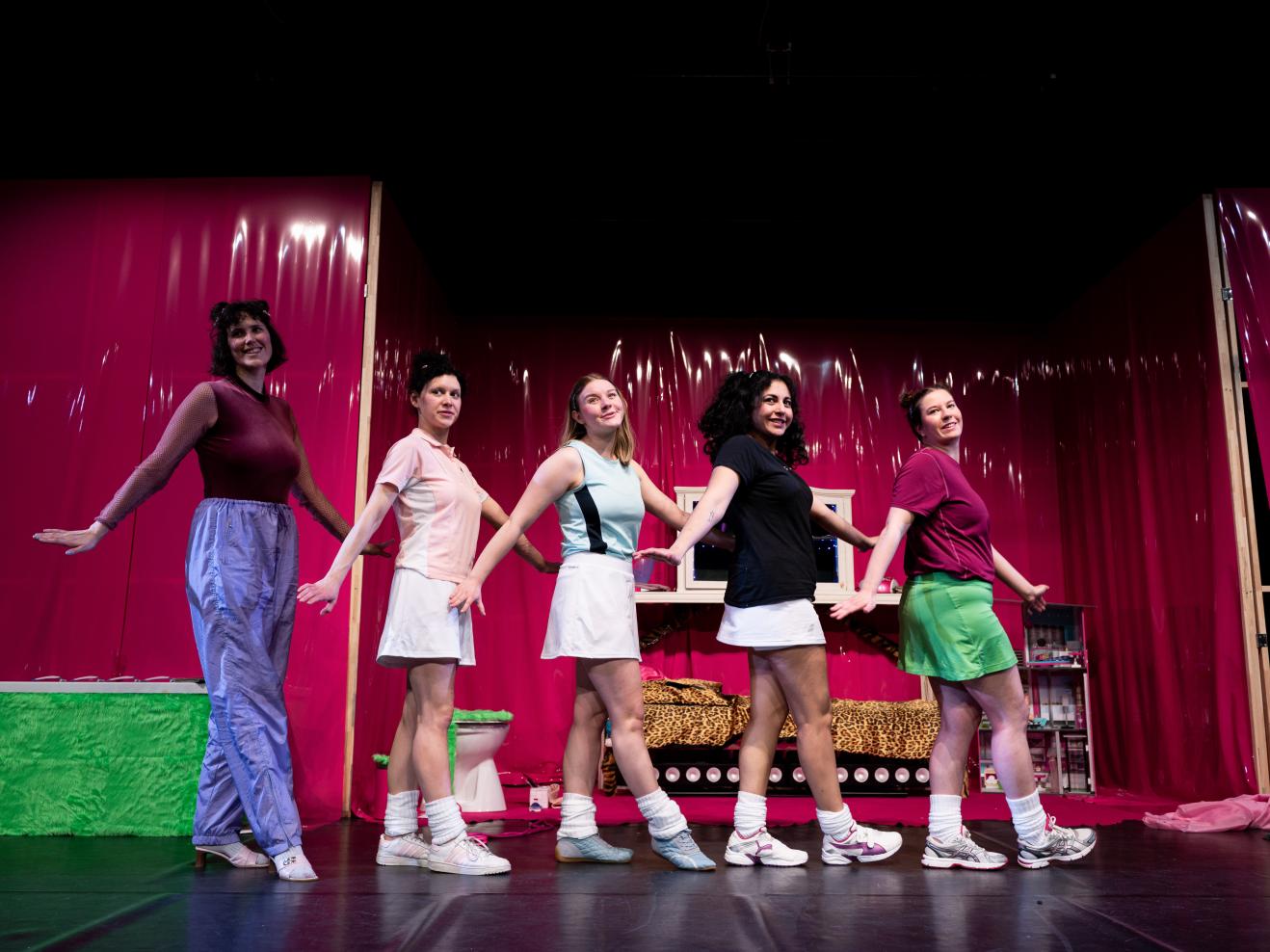 Fünf Frauen in einem pink-bunten Bühnenbild tanzen in einer Reihe.