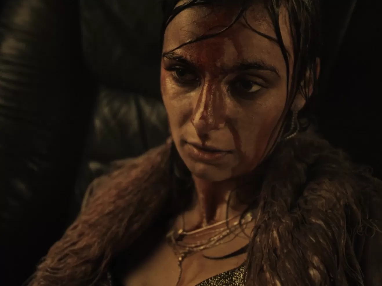 Frau sitzt in einem Auto mit nüchternem Blick und im Gesicht mit Blut bedeckt.