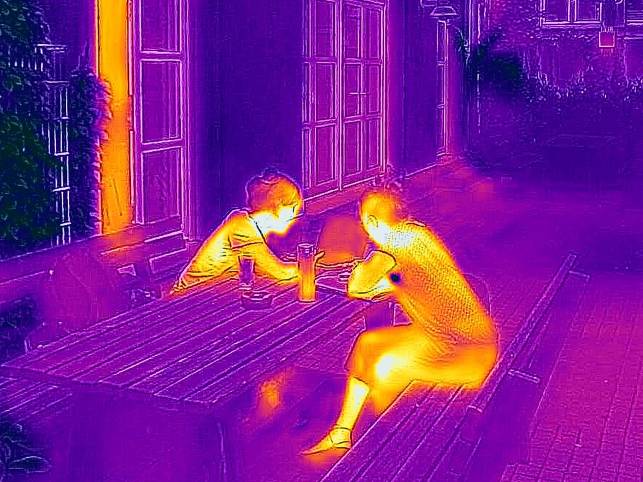 Thermografie-Aufnahme von zwei Personen, die an einem Tisch sitzen und auf einen Laptop schauen.