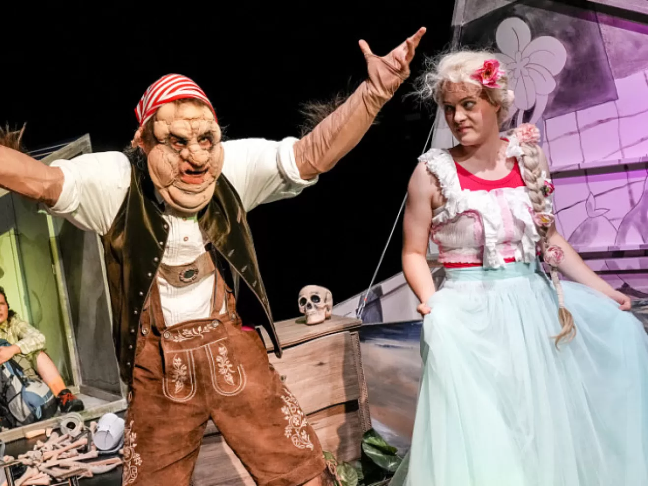 Ein maskierter Mann streckt die Arme aus, von der Seite blickt ihn eine Frau an.