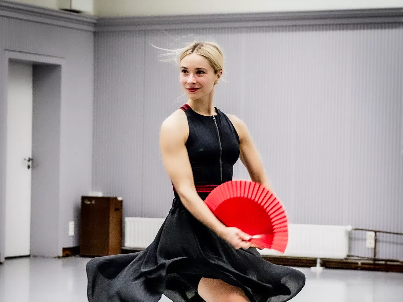 Eine Studentin tanzt im schwarzen Kleid und mit einem roten Fächer in der Hand.