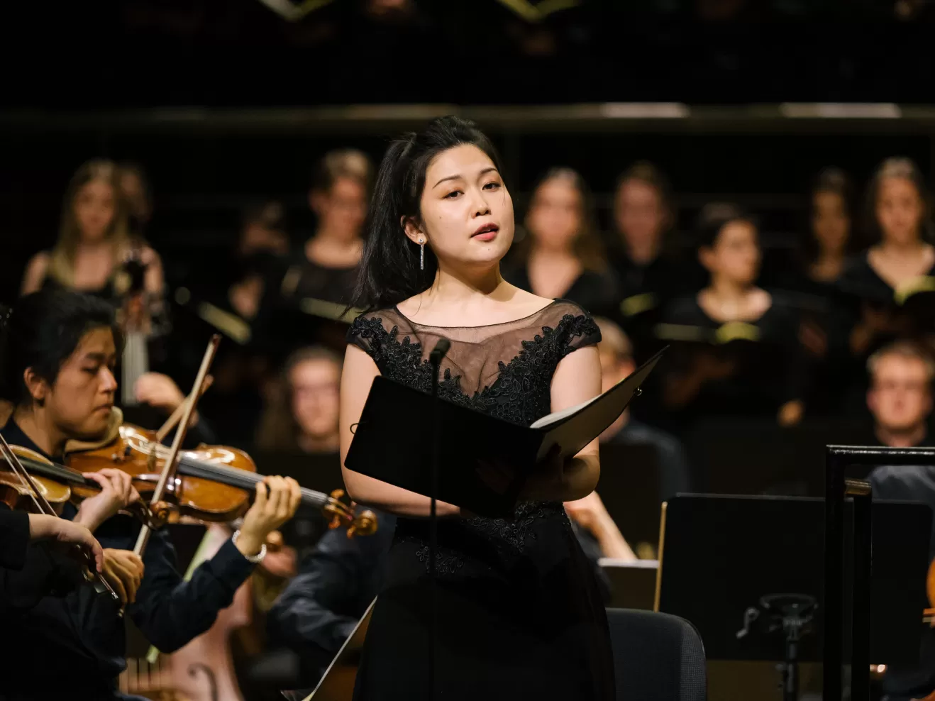 Solo-Sängerin in schwarzem Kleid mit dem HfMDK-Orchester auf der Bühne im Großen Saal
