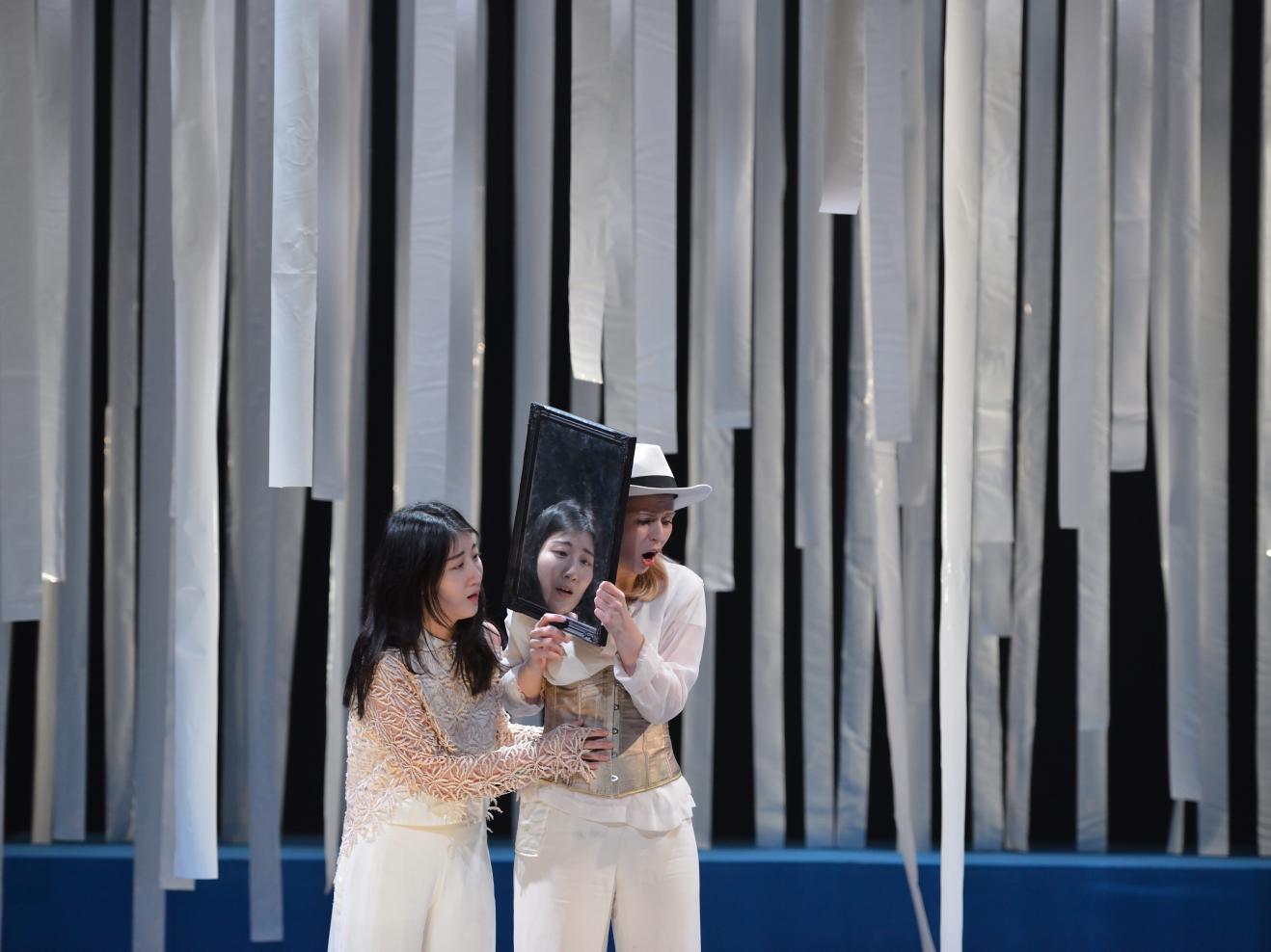 Zwei Musiktheaterdarsteller*innen mit einem Spiegel zwischen ihnen auf der Bühne.