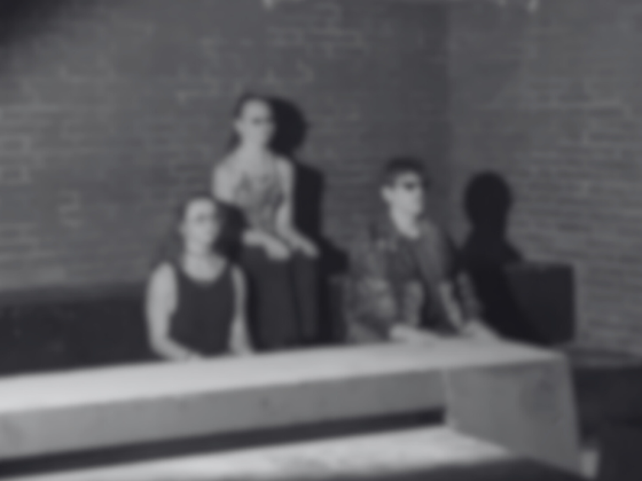Das schwraz-weiß Foto zeigt in Unschärfte drei Personen sitzend vor einer Wand.
