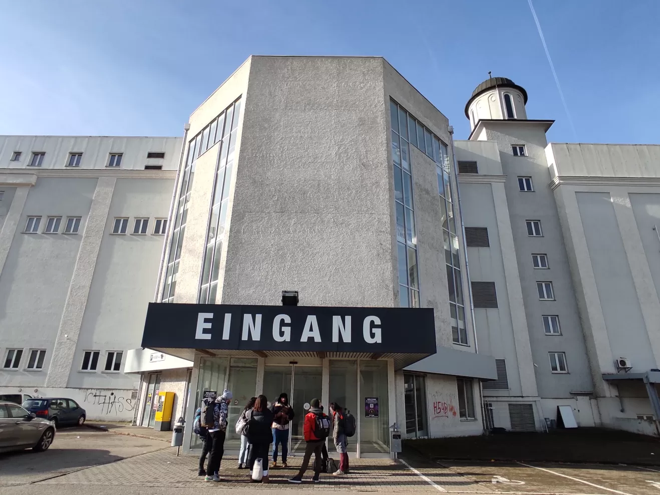 Studierende des Kuratieren-Workshosp im Wintersemester 2023/24 stehen vor einem Gebäude, auf dem groß "Eingang" steht.